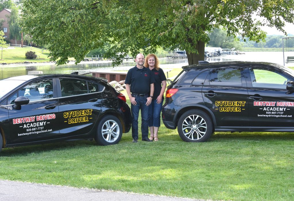 Owners of Bestway Driving Academy next to two cars